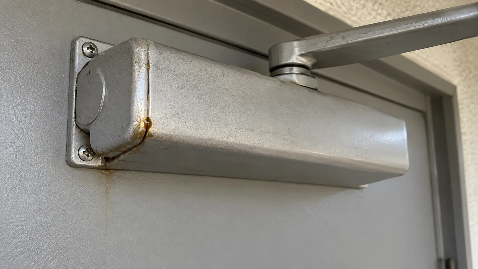 本体の端に油がにじんだ玄関ドアクローザー