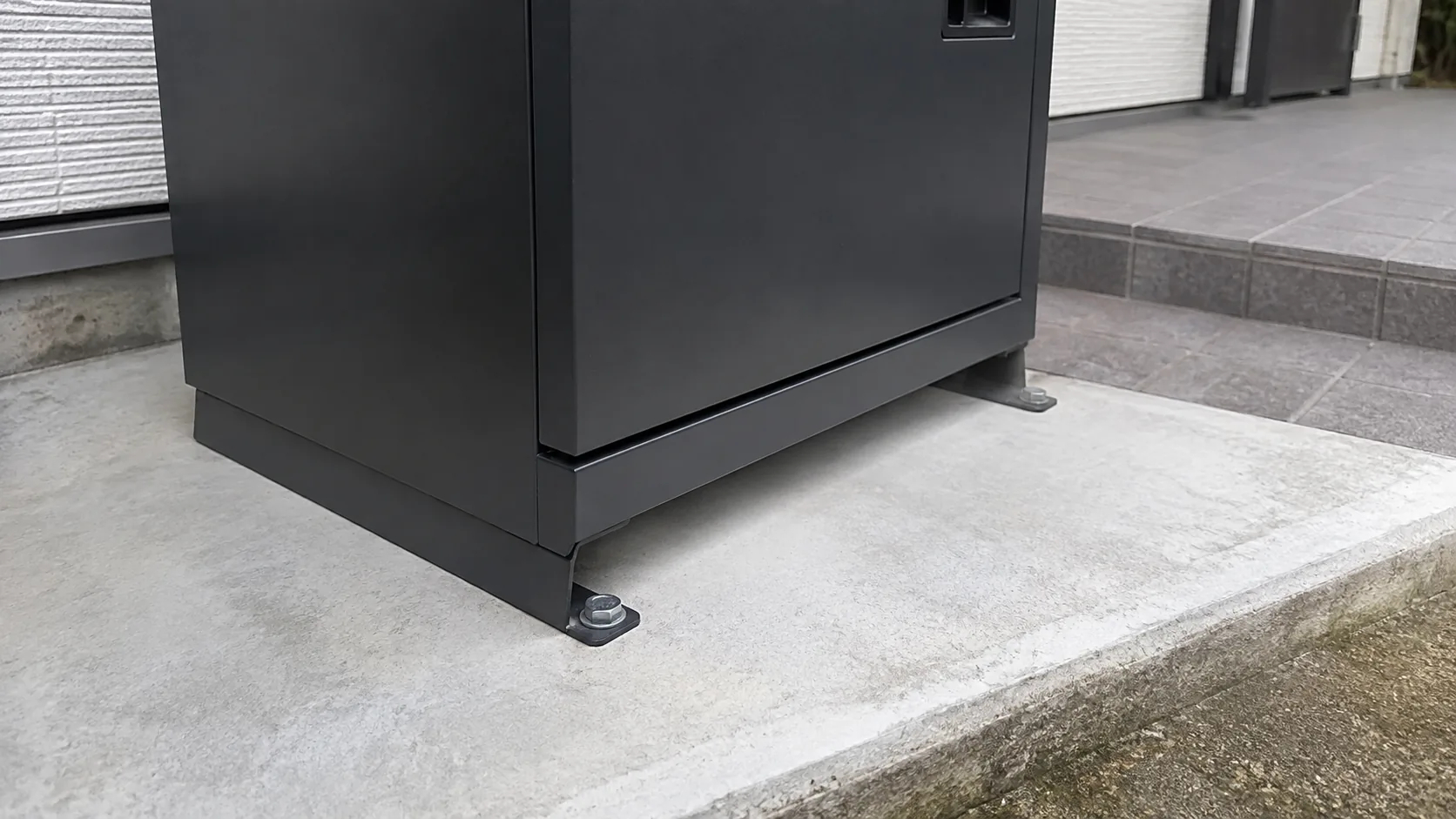 宅配ボックスの台座をコンクリートへ固定した金具とボルト
