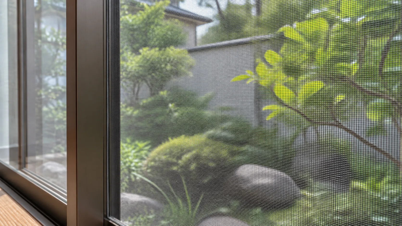 庭の緑を背景にした細かな網目と網戸の縦枠